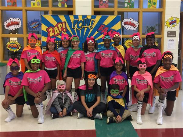 Sawyer Road Cheer club students in hero-themed attire pose together, comic book style POW!, SMASH! and WHAM! signs surrounding